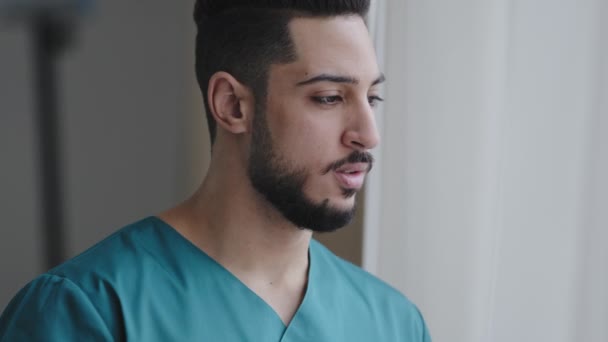 若い受動的ヒスパニック医師男性思慮深いアラビア語の看護師開業医セラピスト外科医は、病院の職場でウィンドウの近くに立つ患者の訪問を待つ悲しい医療マンは検疫を終了することについて考える — ストック動画