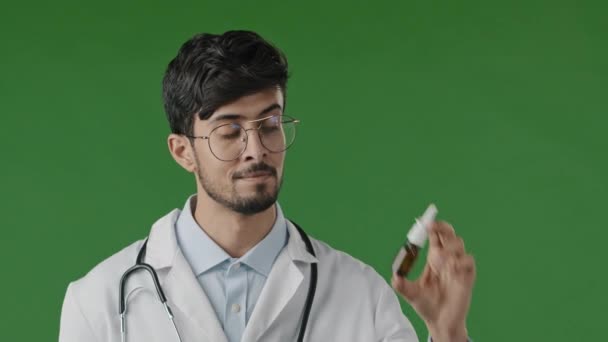 Arabische jonge mannelijke Latijns-Amerikaanse arts in witte jas geïsoleerd in groene studio aanbevelen op camera neusspray geneeskunde remedie vloeistof voor neus herstellen allergie symptomen ziekte advies reclame — Stockvideo