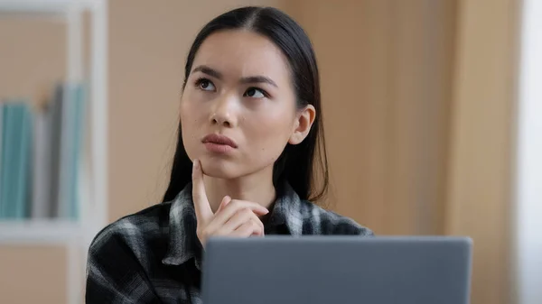 Penser fille étudiante asiatique onéreux portrait de femme fonctionne ordinateur portable faire tâche en ligne à la recherche d'une solution au problème se sent douteux profondément dans les pensées rend la décision pense à la réponse tâche difficile — Photo