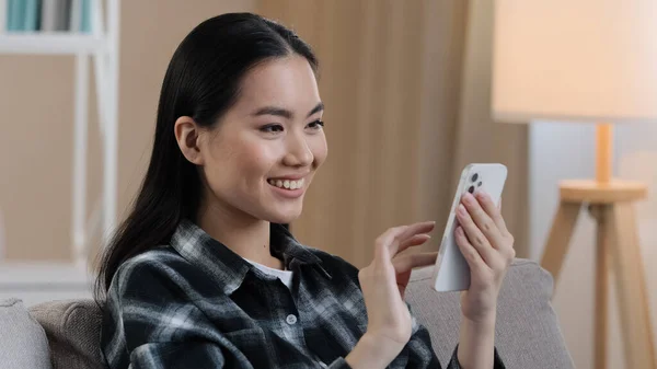 Sourire heureux asiatique femme tapant glisser écran tactile de téléphone coréen fille joyeuse choisir achats en ligne e-commerce app femelle profiter site mobile jouer jeu à la maison suivre message dans les médias sociaux — Photo