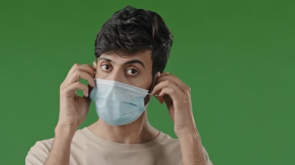ポートレートミレニアル疲れブルネット男患者arab男学生スタンドオン緑の背景取るオフ医療面マスク感じフリー息作るディープ吸い込む削減不足新鮮な空気エンドの流行covid — ストック動画