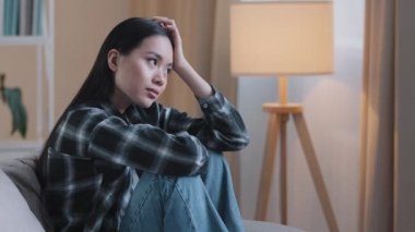 Alone tired boredom sad Asian woman exhausted girl sitting on couch at home feeling unsure unhappy sadness bad feeling mental trouble psychology trouble depressed desperate pensive Korean girl think