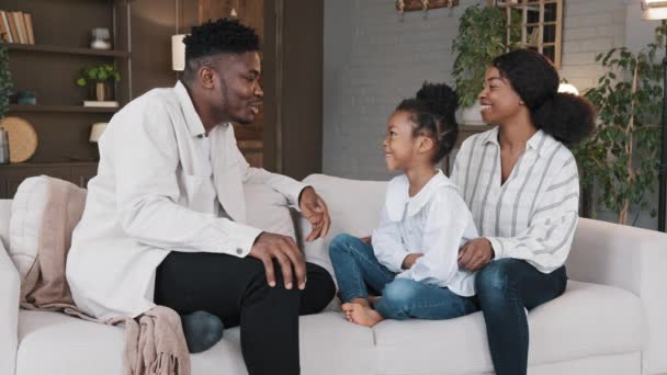 Famille afro-américaine assis sur le canapé dans le salon bavarder conversation occasionnelle rire. Les parents tuteurs multiraciaux naissants parlent de communication avec la nouvelle fille enfant adoptée enfant fille à la maison — Video