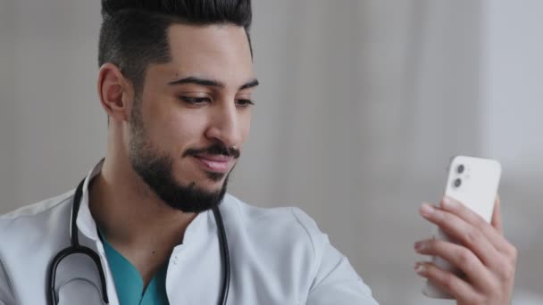 Självsäker kvalificerad läkare manlig arabian läkare använder smartphone social medicinsk app konsultera kunder på nätet i kliniken skåp fjärrkommunikation ge råd telemedicin vård tjänster koncept — Stockvideo