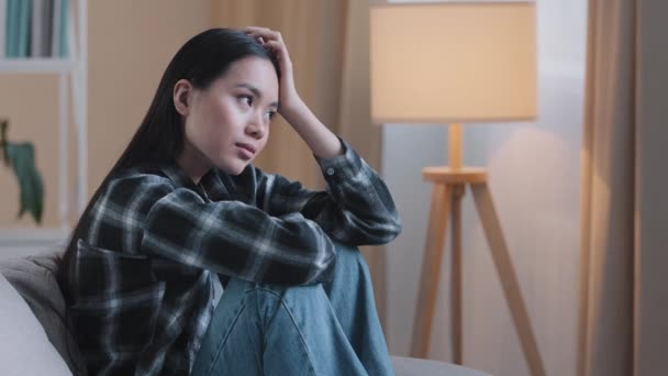 Alone tired boredom sad Asian woman exhausted girl sitting on couch at home feeling unsure unhappy sadness bad feeling mental trouble psychology trouble depressed desperate pensive Korean girl think — Stok Video