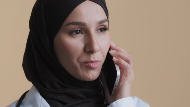 Musulmán árabe joven médico pasante mujer cirujano practicante usar abrigo médico hijab hablar por teléfono celular asesor islámico consultar paciente distante tiene teléfono móvil inalámbrico conversación en la clínica — Vídeo de stock