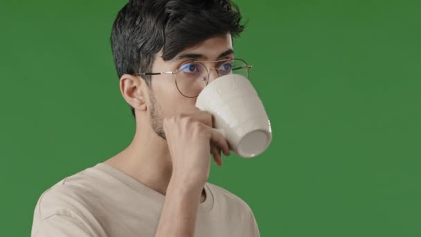 Close up portrait of handsome young arabian guy millennial indian man drink coffee hot herbal tea enjoy weekend hispanic businessman satisfied look into distance daydreaming on green screen background — Stock Video