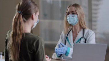 Kafkas kadın doktor kız hemşire, jinekolog, göz doktoru, tıp üniforması ve yüz maskesi uzmanı, hastanede tedavi randevusu alan, tanınmayan hasta bir kadına danışıyor.