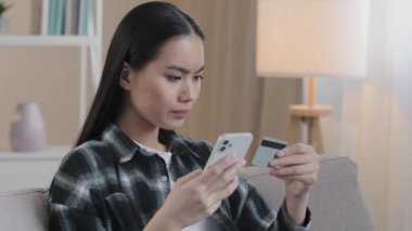 Kharkiv, Ukrayna - 24,12,2021: Asyalı kadının elektronik ödemeyle banka hesabı sorunu engellendi. Cep telefonu kullanmayan kızgın bir kadın kredi kartını çöpe atıyor.