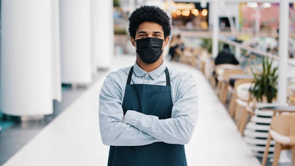 Portrait small business african american cafe worker multiracial man restaurant seller in apron looking camera posing crossing arms waiter in medical mask salesman in crossed hands confident position
