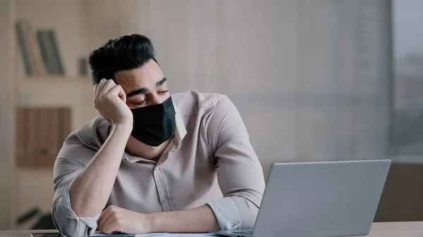 Bored tired hispanic guy worker in medical mask during pandemic coronavirus young business man tired ill worker feel boredom in home office hold head suffering from insomnia thinking about problems — Foto Stock