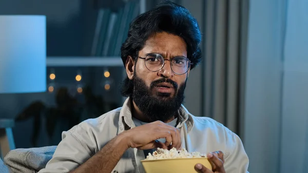 Interesado atento árabe hispano indio barbudo hombre en gafas comer palomitas de maíz viendo serie de televisión película de terror tarde por la noche sensación de miedo conmocionado miedo reacción disgusto horrible thriller —  Fotos de Stock