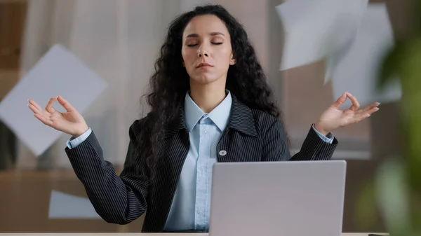 Calm mindful female business woman boss in lotus position taking break meditating background of throwing papers doing breathing yogic practices feeling no stress keeping balance at office workplace