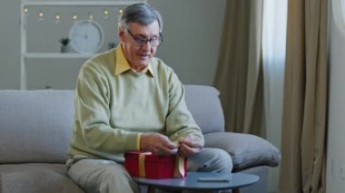Mutlu Kafkasyalı yaşlı adam büyükbaba emeklinin kırmızı hediye kutusunu sarıp kurdele bağlaması. Büyükbaba evde oturarak doğum günü Noel kutlaması için hediye hazırlıyor. Noel tatili. Tebrikler.