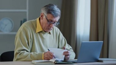 Gözlüklü yaşlı, yaşlı, gözlüklü, internetten bilgi okuyan, not defterindeki bilgilere bakan birden fazla görev yapan Kafkas öğretmeni profesörü. Odaklanmış eski uzaktan çalışan finans analizi