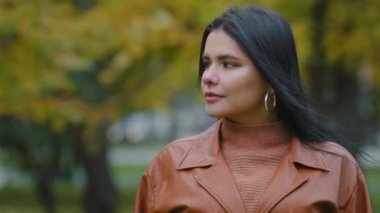 Yakından mutlu, dost canlısı, çekici İspanyol bir kadın parkta durmuş kameraya bakıyor, gülümsüyor, flört ediyor, güzel, mutlu, dişlek, açık havada poz veren beyaz bir kız modeli.