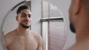 Aynada kendine güvenen, 30 'lu yaşların tıraşsız adamı gülümseyen erkek yansıması. Hey sen işaret parmağını, banyo yapmış çıplak Arap kızılderili adama, dişlek sakallı gülümseyen milenyum gülüşüne doğru sallıyorsun.