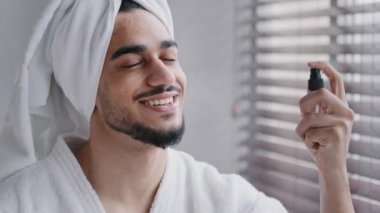 Kafasında beyaz banyo havlusu olan komik İspanyol sakallı Hintli adam banyoda güzellik prosedürleri mükemmel cilt bakımı erkek nemlendirici yüz spreyi kullanıyor. Yüksek