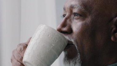 Afro-Amerikan 60 'lı yılların yalnız iş adamı, kahve fincanından çay içiyor pencereden dışarı bakıyor, hayal kuruyor, dinleniyor, ev ofisinin güzel kokulu içkilerinden keyif alıyor.
