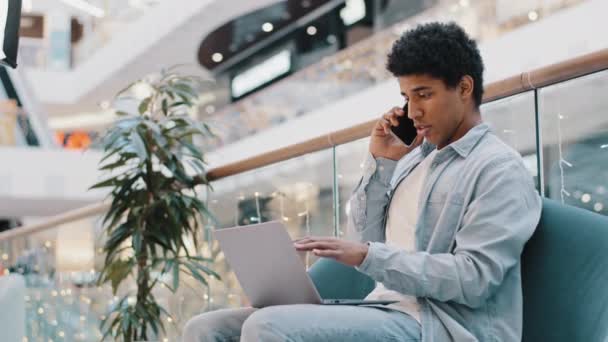 アフリカを中心に30代のフリーランスのビジネスマンがノートパソコンの画面を見て説明を指すビジネスコールの交渉の議論を行います 携帯電話のコンサルティングクライアントに話す深刻な男 — ストック動画