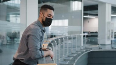 Yakın plan şirket çalışanı, patron patron, iş adamı, siyah tıbbi maskeli Arap bir adam ofis salonunda dikilip dinlenme projesini düşünüyor.