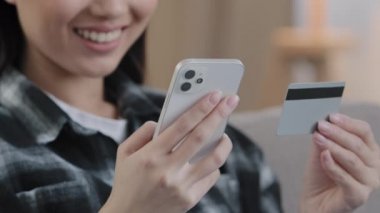 Yakın plan tanınmayan Asyalı kadın online cep telefonu servisi ödüyor. Kadın eller banka kredi kartı ve telefon tutuyor internet ödemeleri yapıyor e-ticaret alışverişi yapıyor internet alışveriş uygulaması siparişinde