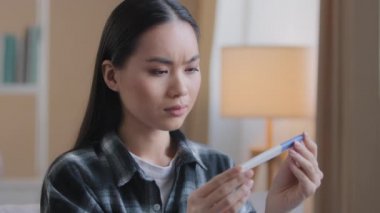 Bekleyen kafası karışmış Asyalı kadın hamilelik testi sonucu planlanmamış çocukları için endişeleniyor. Mutsuz hamile Koreli kadın, istenmeyen hamilelik reaksiyonu yüzünden evinde oturuyor.