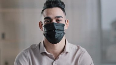 Tıbbi maskeli Latin kökenli, etnik erkek işadamı. Koronavirüs salgınından koruyor. Kapalı alanda baş parmak gösteriyor.