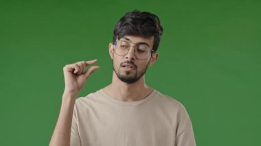 Hayal kırıklığına uğramış esmer Arap adam parmaklarıyla küçük bir jest yapıyor. Tatmin olmamış adam küçük boyutta, düşük oranlı ölçü gösteriyor. Küçük ölçekli, kapalı alanda yeşil arka planda izole edilmiş duruyor.