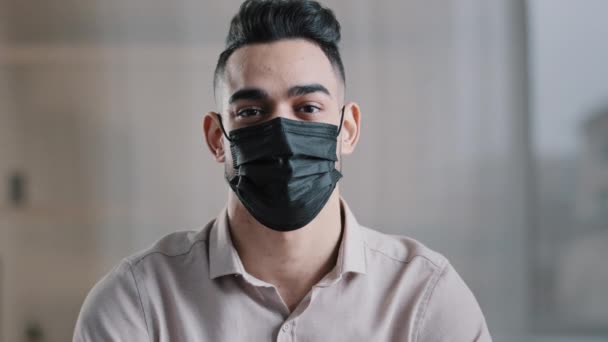 医者のマスクの民族男性学生のビジネスマンのヒスパニック系の男は ジェスチャーのような親指を示す室内でポーズコロナウイルスの発生から保護する健康予防接種をお勧めしますウイルスを防ぐ — ストック動画