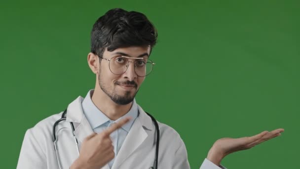 積極的なアラビア語ハンサムな男性医師インドの男性歯科医は 左側に空白のスペースポイントインデックス指を使用することをお勧めします想像上のオブジェクトを提供緑の背景に隔離された良い選択を示す — ストック動画