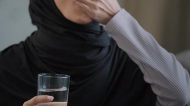 Müslüman kadın tesettüre girmiş Arap hasta kadın baş ağrısından aldığı hapları tutuyor. Vitamin hapı içiyor. Bir bardak mineral ferahlatıcı suyla aspirin koyuyor.