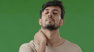 Yorgun, genç, Hintli Arap bir adamın portresi. Aşırı çalışan, fiziksel rahatsızlık hisseden, masaj yapan, kasları gerilen, boynu ağrıyan, yeşil stüdyoda duran, omuzları ağrıyan bir adamın portresi.