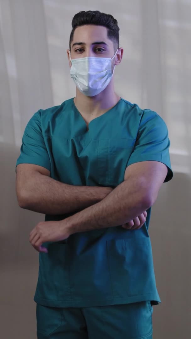 垂直ビューパニック男性看護師男性は 訪問患者のために待っている診療所病院で腕を組んでポーズカメラで均一な表情で医療用マスク医師を着用緊急光の上にCovid 19スタンド — ストック動画