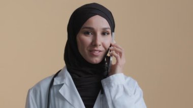 Müslüman doktor genç intörn Arap kadın cerrah tesettür içinde stajyer hasta kadın danışman ile cep telefonuyla tıbbi önlük giyin uzak sanal mobil iletişim sağlık konseptine danışın
