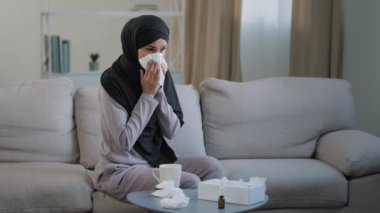 Hasta Arap Müslüman genç, tesettürlü sağlıksız kadın burun gribi, mevsimsel alerji hapşırığı, kağıt peçete semptomlarına burun sümkürme, sıcak çay içme, kendini izole etme, evde otur.