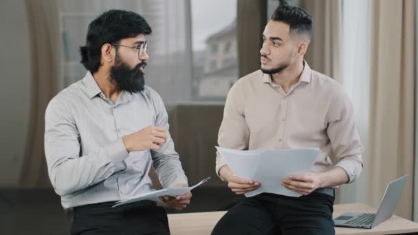 多种族的商人伙伴坐在办公桌前 惊慌失措的专家咨询阿拉伯男性同事持有一堆堆书面文件 讨论金融数据保险合同团队合作的概念 — 图库视频影像