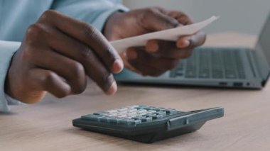 Genç Afrikalı kimliği belirsiz adam bankacı muhasebeci ödeme faturasını elinde tutuyor aylık bütçe hesaplama makinesi hesaplama maliyetleri hesaplıyor kredi dengesi indirimi indirimi faturası ev ofisinde oturuyor