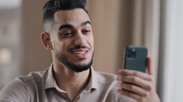 幸せな若いヒスパニック男ビジネスマンハンサムな男フリーランサースマートフォンでのビデオ通話による笑顔の話挨拶リモート友人は 仮想会議距離モバイルチャット通信無線接続を持っています — ストック動画