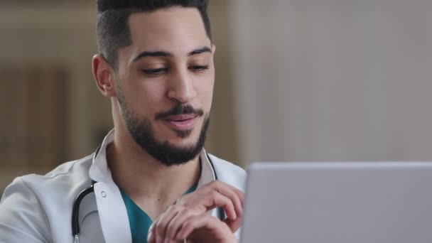 若い男性のヒスパニック看護師医師白衣のアラブ医療アドバイザーは Webカメラのジェスチャーでデジタル技術の話を使用して ラップトップ上でオンライン仮想相談ビデオチャットウェビナーを提供します — ストック動画