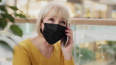 Yakın planda, tıbbi maskeli, ciddi, beyaz bir iş kadını cep telefonuyla konuşuyor iş konularını görüşüyorlar akıllı telefon konuşmalarını kullanarak uzaktan arkadaşlarıyla konuşuyorlar.