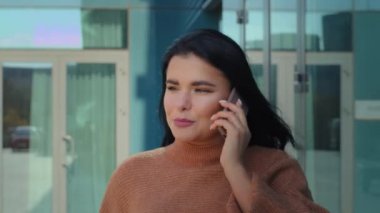 Kendine güvenen başarılı iş kadını dışarıda telefonla konuşuyor zarif bir bayanı arıyor arka plandaki ofis binasında akıllı telefon kullanarak iletişim kuruyor.
