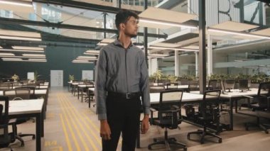 Portre gülümseyen esmer, yakışıklı, Hintli, Arap, genç, erkek, iş adamı, lider, pazarlamacı, modern ofiste kollarını kavuşturup kameraya bakarak tatmin edici pozlar veriyor.