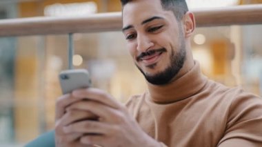 Yakın plan genç Arap adam elinde telefonla ekrandaki akıllı telefona bakıyor gülümsüyor güzel e-posta mesajları alıyor arkadaşlık sitelerinde geziniyor sosyal ağ ücretsiz kablosuz internetin keyfini çıkarıyor çevrimiçi mağazada siparişi onaylıyor
