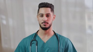 Kendine güvenen Arap asıllı, İspanyol asıllı, stajyer, erkek hemşire, doktor, steteskop ile tıbbi üniforma giyiyor. Klinik hastanesinde kamera sağlık servisi acil durum ışığı geçmişine bakıyor.