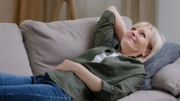 Mutlu, orta yaşlı, düşünceli, düşünceli bir kadın evdeki kanepede dinleniyor. Huzurlu bir ruh hali, uykulu, tembel, yaşlı, olgun bir kadın rüyası. Oturma odasında rahat bir kanepede uzanıyor. Stres yok.