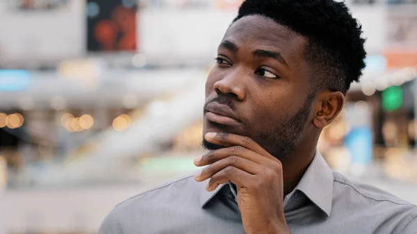 Close-up puzzled concentrated pensive serious african american young man looking away keeps hand on chin thinks solves problem comes up with new opportunities idea startup dreaming plunged thoughts