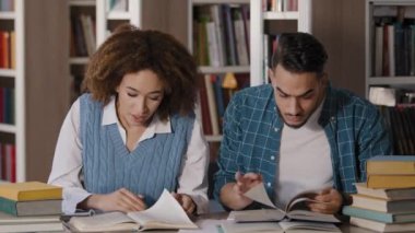 Öğrenci erkek ve kız sınıf arkadaşları kütüphanede oturup okul projesinde birlikte çalışarak gerekli bilgileri arıyorlar. Üniversitede sınava hazırlanmak için kitap okuyorlar.