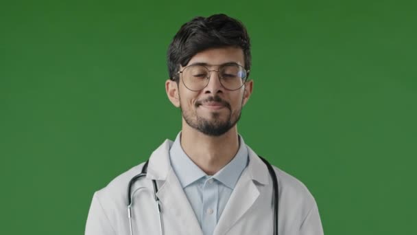 专业医生身穿白衣 配上听诊器 看着镜头 站在绿色工作室背景中 与外界隔绝的男性医疗顾问的形象 — 图库视频影像
