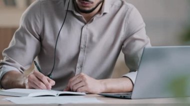 Bilinmeyen adamı kapat yazar öğrenci resepsiyonist kulaklık tak bilgisayardaki eğitici konferans webinar 'ını dinle ödev bilgilerini yaz kitap organizatörüne notlar yaz